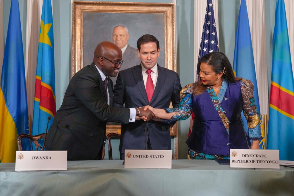 Foreign ministers of DRC and Rwanda shake hands while signing peace documents as US Secretary of State looks on in Washington ceremony.