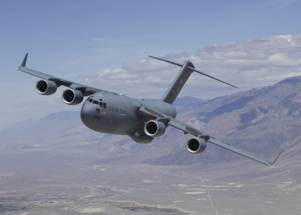 A C-17 Globemaster III opens its rear ramp to release aid bundles over a crowded Gaza neighborhood.