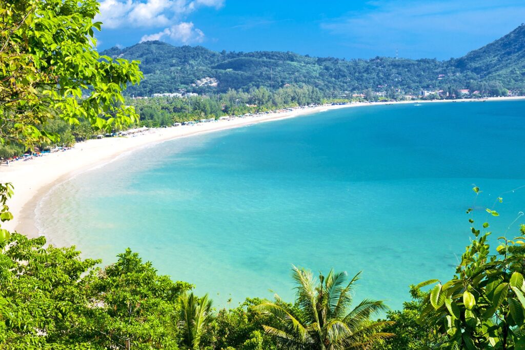 Russian expats walking on a Phuket beach with luxury condos and palm trees in the background.