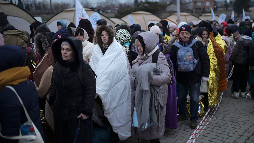 Ukrainian refugees carrying bags cross a border checkpoint into eastern Europe, fleeing Russian strikes in western Ukraine.